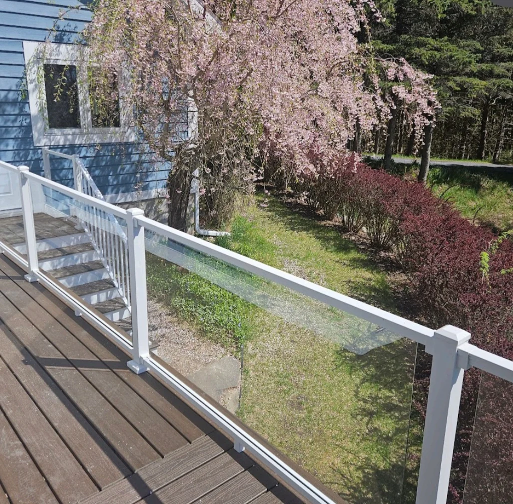 Residential deck with white posts and clear railing panels beside a landscaped garden.