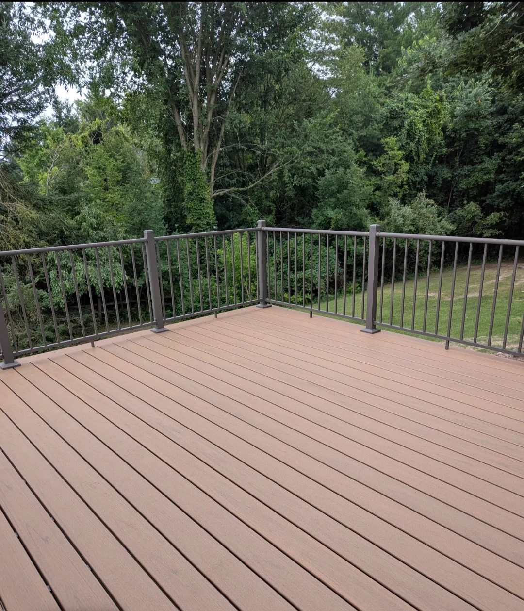 Open residential deck with brown boards and dark railing overlooking trees.