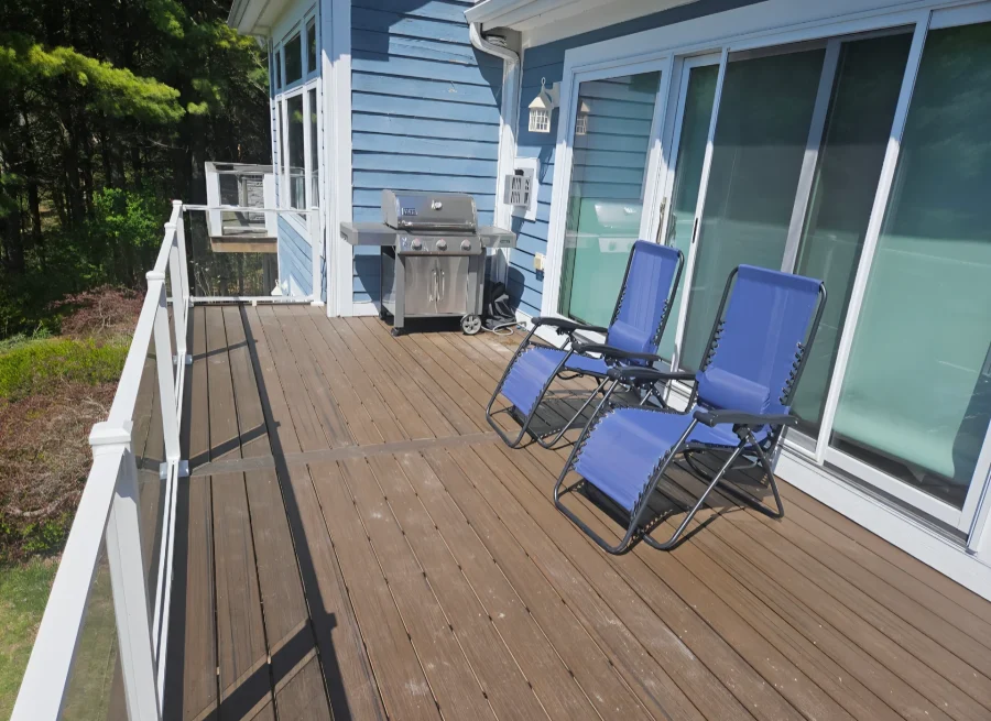 Deck beside a blue house with white railing and outdoor seating.