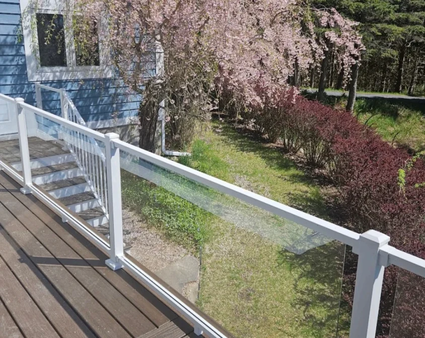 Deck with white posts and clear railing panels beside a landscaped yard.