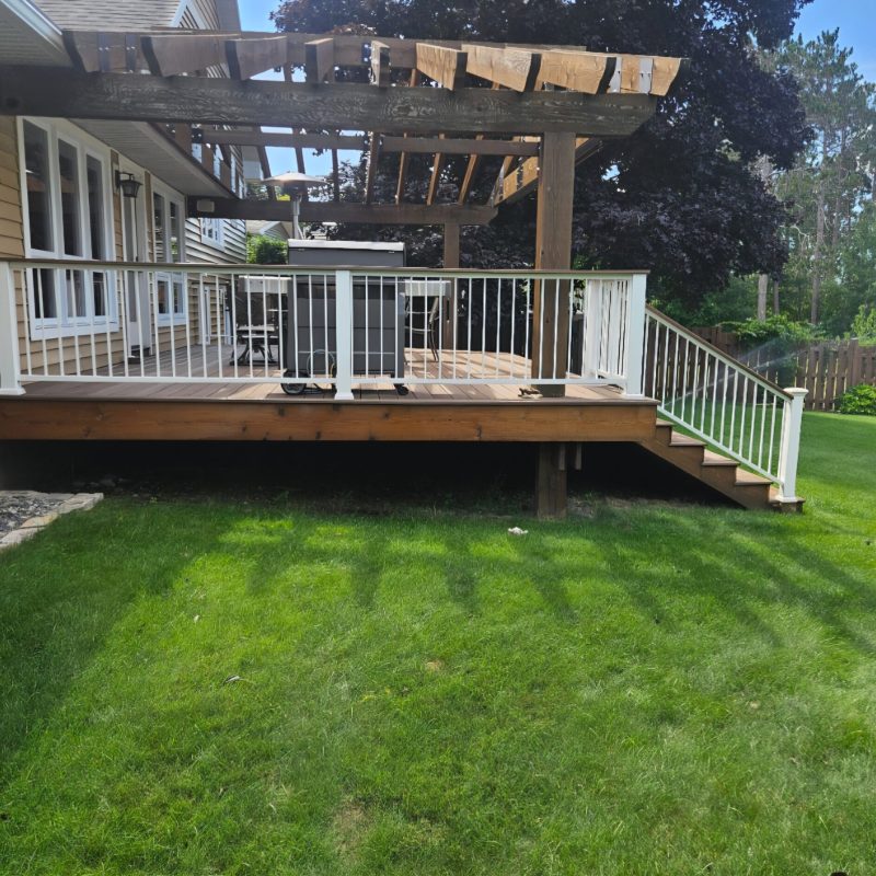 Deck with white railing, steps, and a timber pergola beside a house.