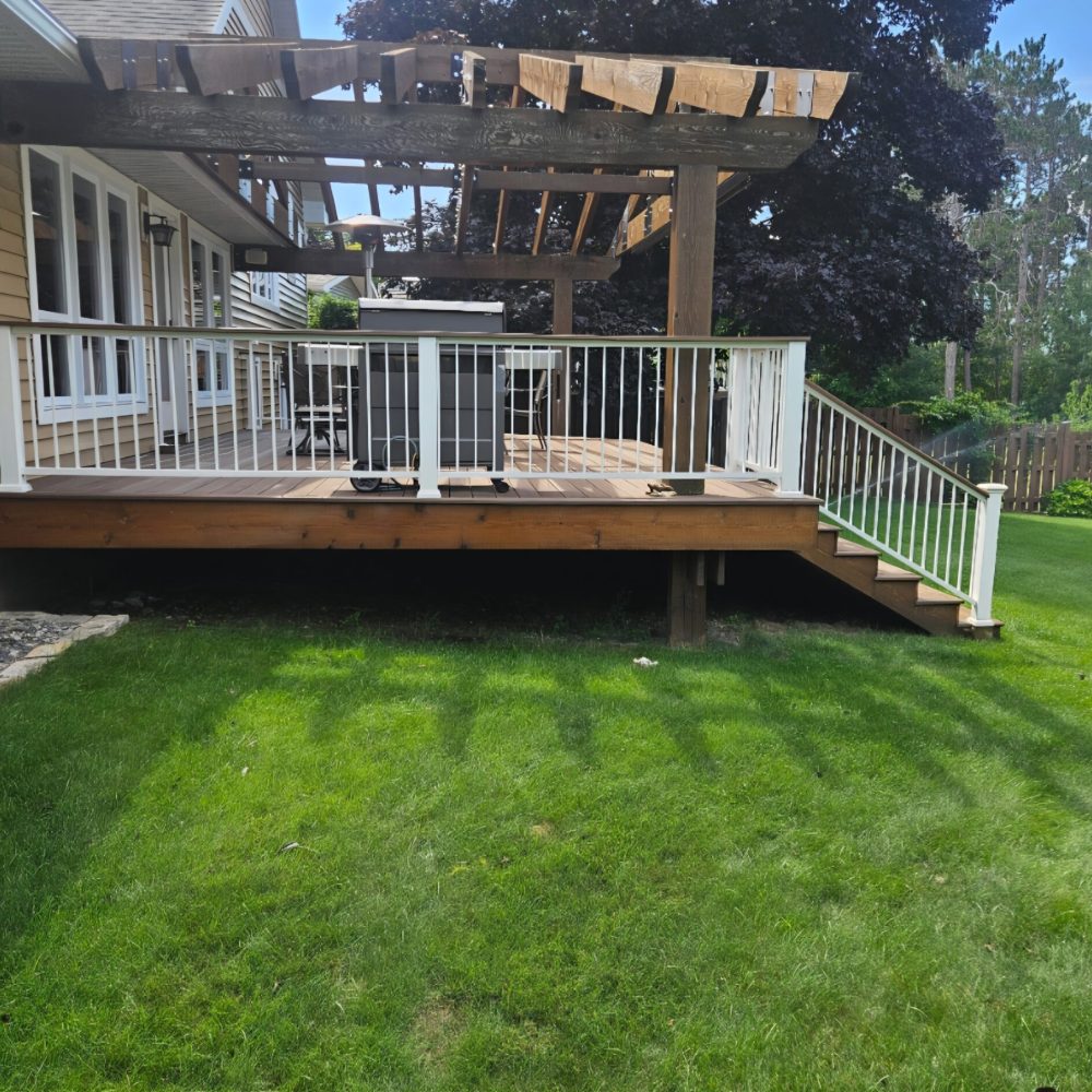 Deck with white railing, steps, and a timber pergola beside a house.
